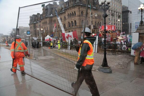 Workers carry sections of mesh fencing to the perimeter of Parliament Hill in downtown Ottawa on Feb. 17, 2022. (Richard Moore/The Epoch Times)