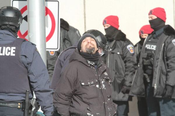 An arrested man enjoys the sunshine while waiting to be processed by police in Ottawa on Feb. 18, 2022. (Richard Moore/The Epoch Times)