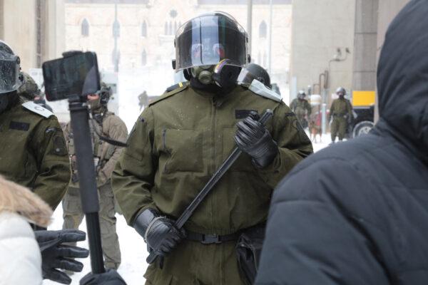 Canadian police in helmets and carrying long batons form a line near Parliament Hill in Ottawa on Feb. 20, 2022. (Richard Moore/The Epoch Times)