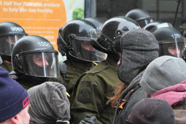 Protesters face-off against Canadian police in helmets and carrying long batons near Parliament Hill in Ottawa on Feb. 20, 2022. (Richard Moore/The Epoch Times)