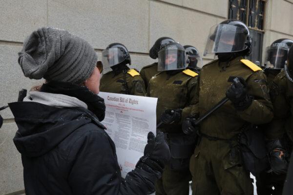 A protester stands with the Canadian Bill of Rights in front of police near Parliament Hill in Ottawa on Feb. 20, 2022. (Richard Moore/The Epoch Times)