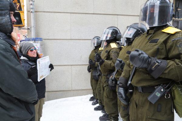 Protesters stand in front of police in helmets and carrying long batons near Parliament Hill in Ottawa on Feb. 20, 2022. (Richard Moore/The Epoch Times)