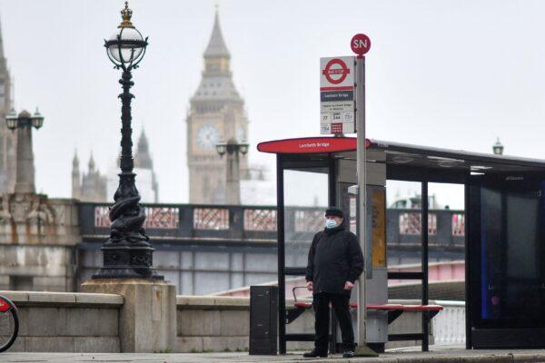 A commuter wearing a mask waits at a bus stop near the Elizabeth Tower, commonly known as Big Ben, at the Palace of Westminster in London, on Feb. 16, 2022. (Justin Tallis /AFP via Getty Images)