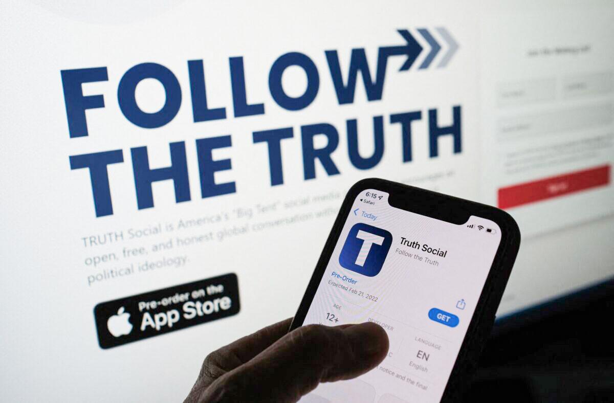 This illustration photo shows a person checking the app store on a smartphone for "Truth Social"—owned by Trump Media & Technology Group—with its website on a computer screen in the background, in Los Angeles, on Oct. 20, 2021. (Chris Delmas/AFP via Getty Images)
