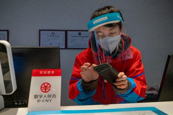 A worker at the front desk of Prince Ski Town Hotel checks the phone behind a sign saying "digital renminbi (e-CNY) is accepted" in Zhangjiakou, China on Dec. 04, 2021. (Andrea Verdelli/Getty Images)