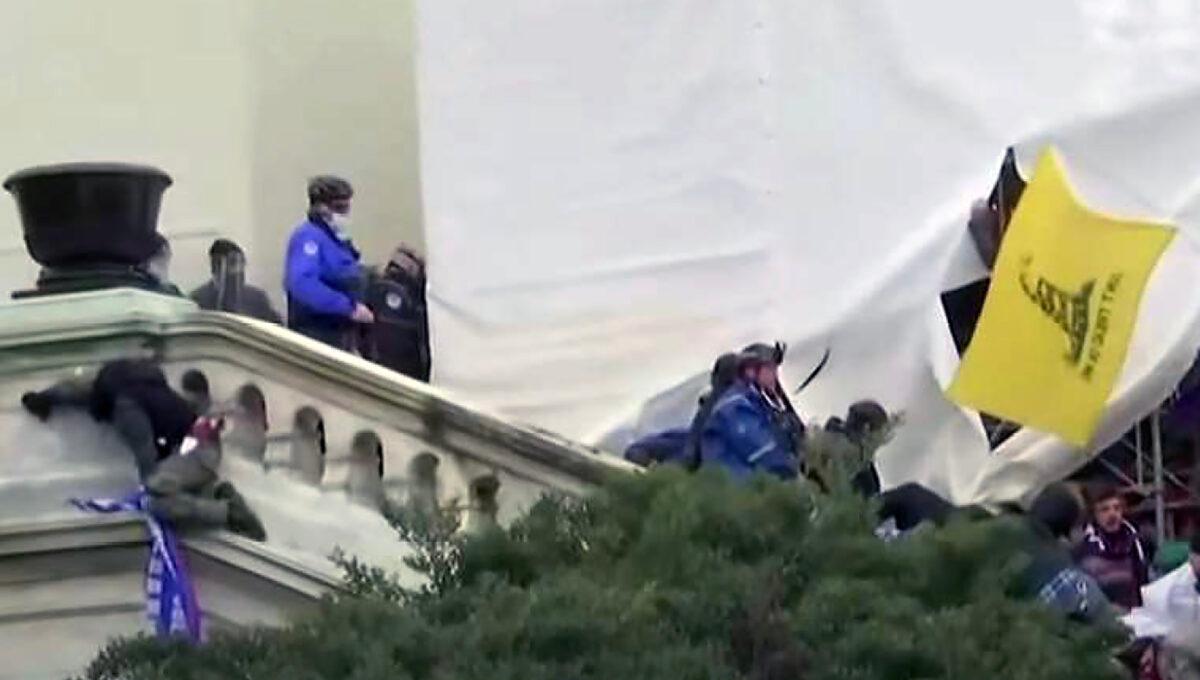 Guy Wesley Reffitt is shown descending the Upper West Terrace stairs at the U.S. Capitol on Jan. 6, 2021. On the ledge at left is Derrick Vargo, who says a police officer pushed him off the 20-foot-high wall. (U.S. Department of Justice/Screenshot via The Epoch Times)