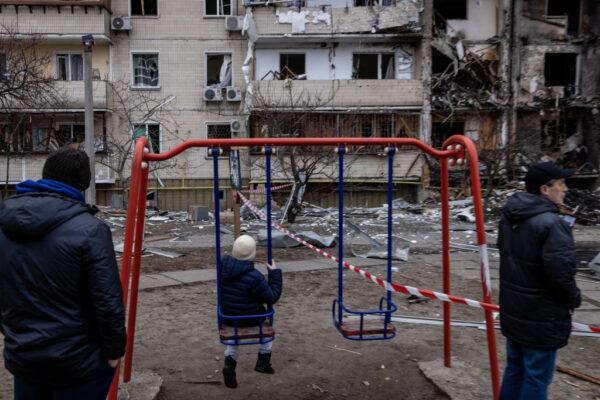 A boy plays on a swing in front of a damaged residential block hit by an early morning missile strike in Kyiv, Ukraine, on Feb. 25, 2022. (Chris McGrath/Getty Images)
