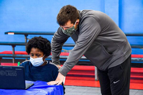 A YMCA staff member assists a child as they attend online classes at a learning hub inside the Crenshaw Family YMCA during the Covid-19 pandemic in Los Angeles on February 17, 2021. (Patrick T. Fallon/AFP via Getty Images)