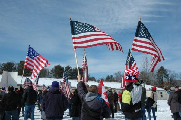 A group of New England truckers lift their American flags in unison at a rally to show support for convoy. (Alice Giordano/The Epoch Times)