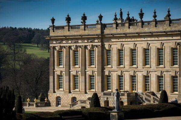 Elaborately carved stonework appears above the windows on the left of the south façade. A roofline balustrade, or railing, is topped with sculpted torches and urns that extend the façade and draw the eye upward. (Chatsworth House Trust)