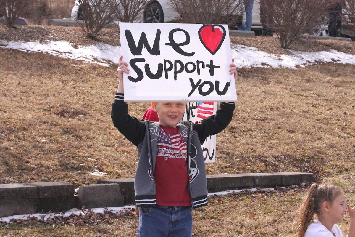 A child holds a sign in support of the People's Convoy, a group of trucks and other vehicles, in Missouri, on Feb. 28, 2022. (Enrico Trigoso/The Epoch Times)