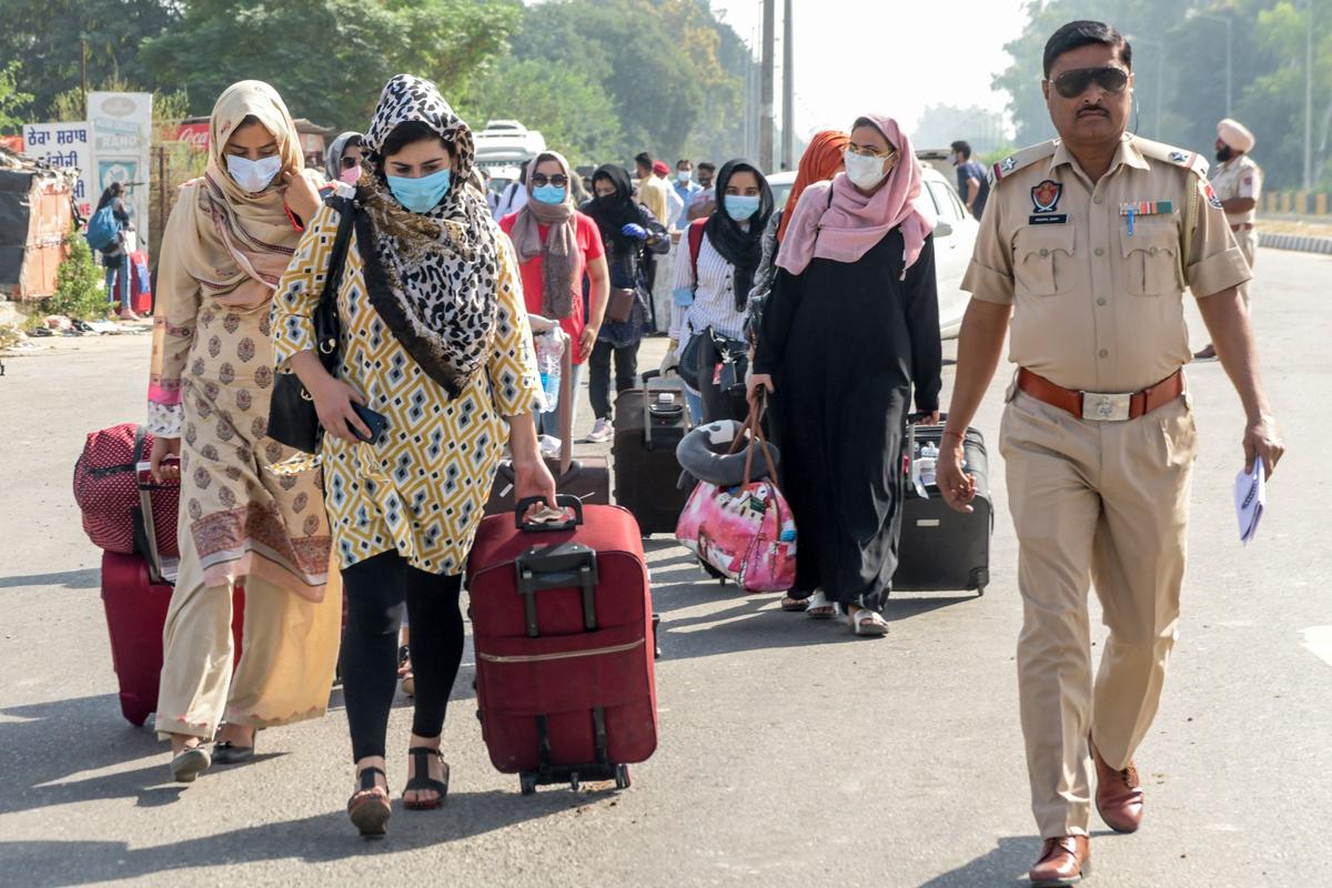Police personnel (R) escort Indian Kashmiri students carrying their belongings as they prepare to return to their colleges in Pakistan, at the India–Pakistan Attari–Wagah border post about 35 kilometers from Amritsar, India, on Sept. 30, 2020. (Narinder Nanu/AFP via Getty Images)