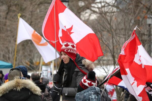 A protester carrying a large Canadian flag was seen at Queen's Park in downtown Toronto as part of a nation-wide "freedom chain" movement stretching across Canada on March 5, 2022. (Annika Wang/The Epoch Times)