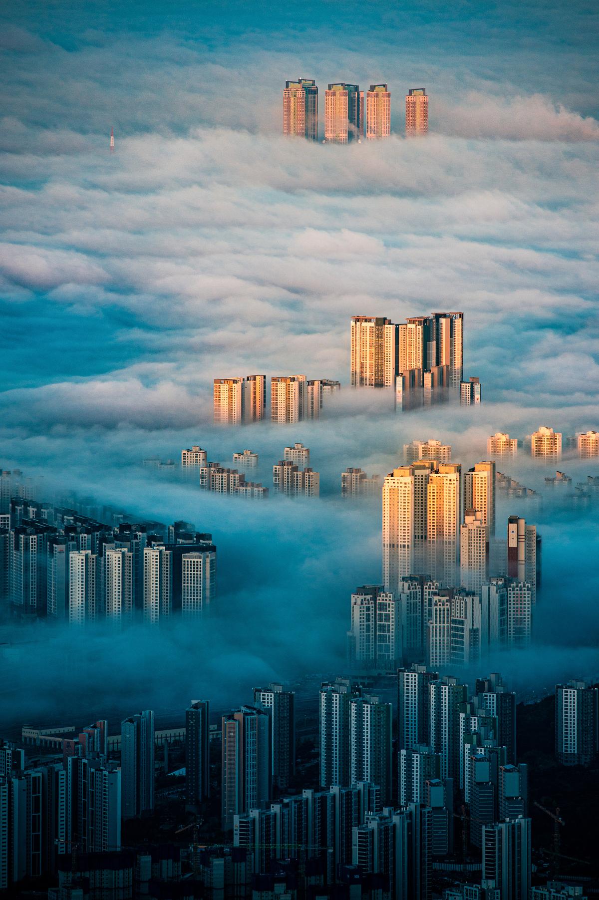 "A City Among the Clouds" by Wonyoung Choi, Korea, Republic Of; “This is a photograph from Bukhansan Mountain in Seoul, South Korea. Lots of people climb the mountain to view the sunrise, but it’s a rare sight to see the city covered in clouds as the sun rises. I've gone there many times and was lucky to finally see it. I feel gratitude towards Mother Nature for changing Seoul's architecture from monotonous to colorful.” (© Wonyoung Choi, Korea (Republic of), Winner, National Awards, Architecture, 2022 Sony World Photography Awards)