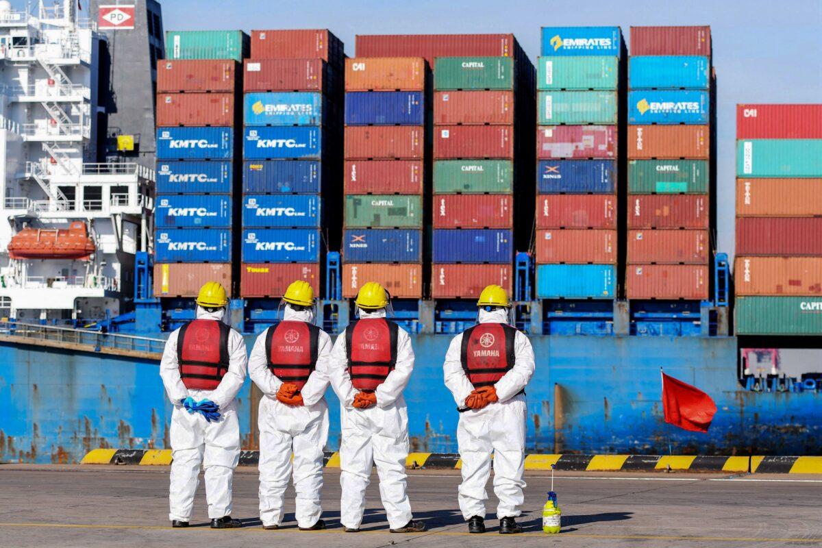 Employees wearing personal protective equipment (PPE) look on by a cargo ship at a port in Qingdao, in China's eastern Shandong Province, on Jan. 14, 2022. (STR/AFP via Getty Images)
