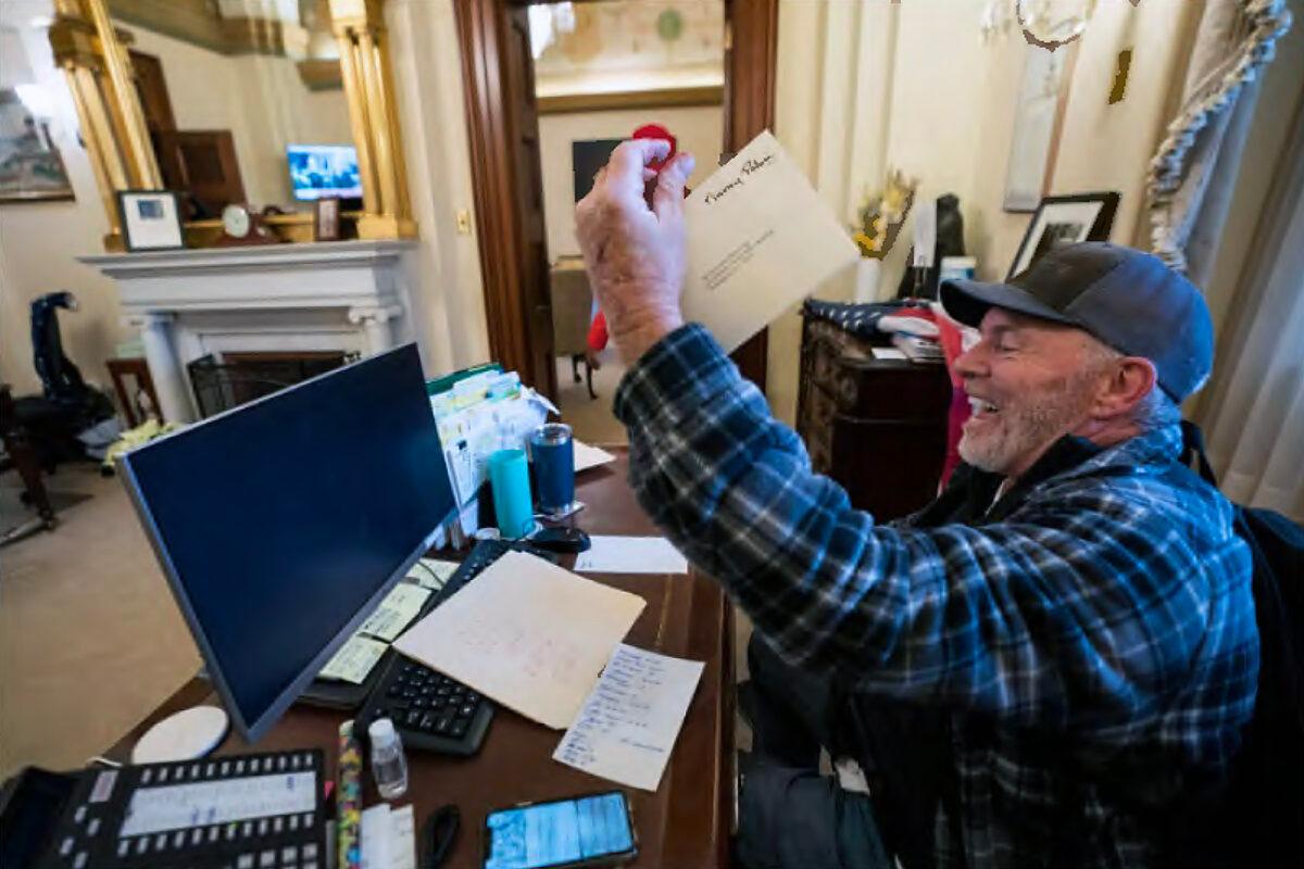 Richard "Bigo" Barnett holds up an envelope he took from House Speaker Nancy Pelosi's office on Jan. 6, 2021. He said he took the envelope because he got blood on it from a cut finger. (U.S. Department of Justice/Screenshot via The Epoch Times)