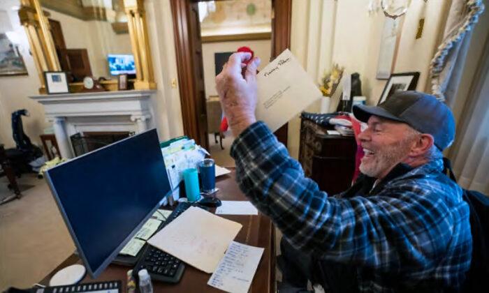 Richard "Bigo" Barnett holds up an envelope he took from House Speaker Nancy Pelosi's office on Jan. 6, 2021. He said he took the envelope because he got blood on it from a cut finger. (U.S. Department of Justice/Screenshot via The Epoch Times)