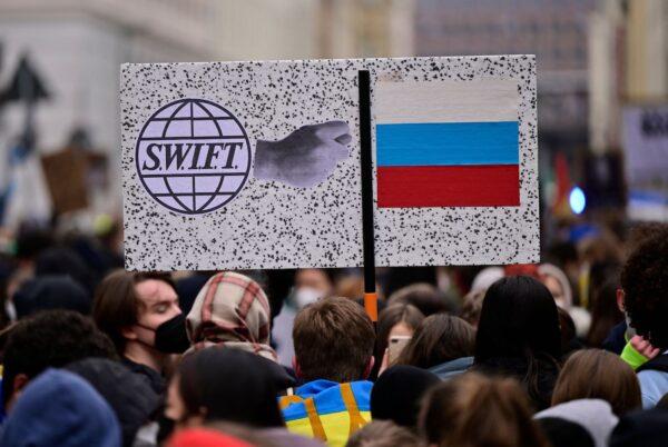 Supporters of the Fridays for Future movement hold a sign with the logo of bank messaging system SWIFT and the Russian flag during a demonstration against the war in Ukraine on March 3, 2022, in Berlin. (John MacDougall/AFP via Getty Images)