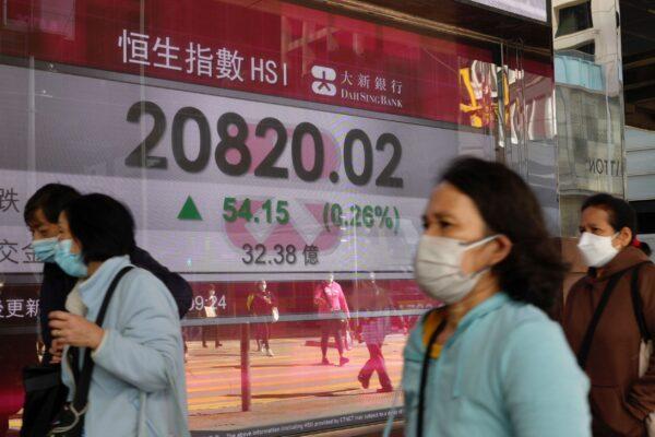 People walk past a bank's electronic board showing the Hong Kong share index at Hong Kong Stock Exchange, on March 9, 2022. (Vincent Yu/AP Photo)
