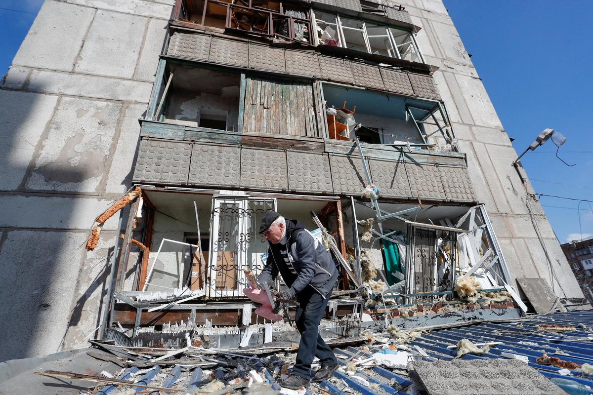 A man removes debris outside a residential building damaged by shelling during the Ukraine-Russia conflict in the separatist-controlled town of Makeyevka (Makiivka) outside Donetsk, Ukraine, on March 16, 2022. (Alexander Ermochenko/Reuters)