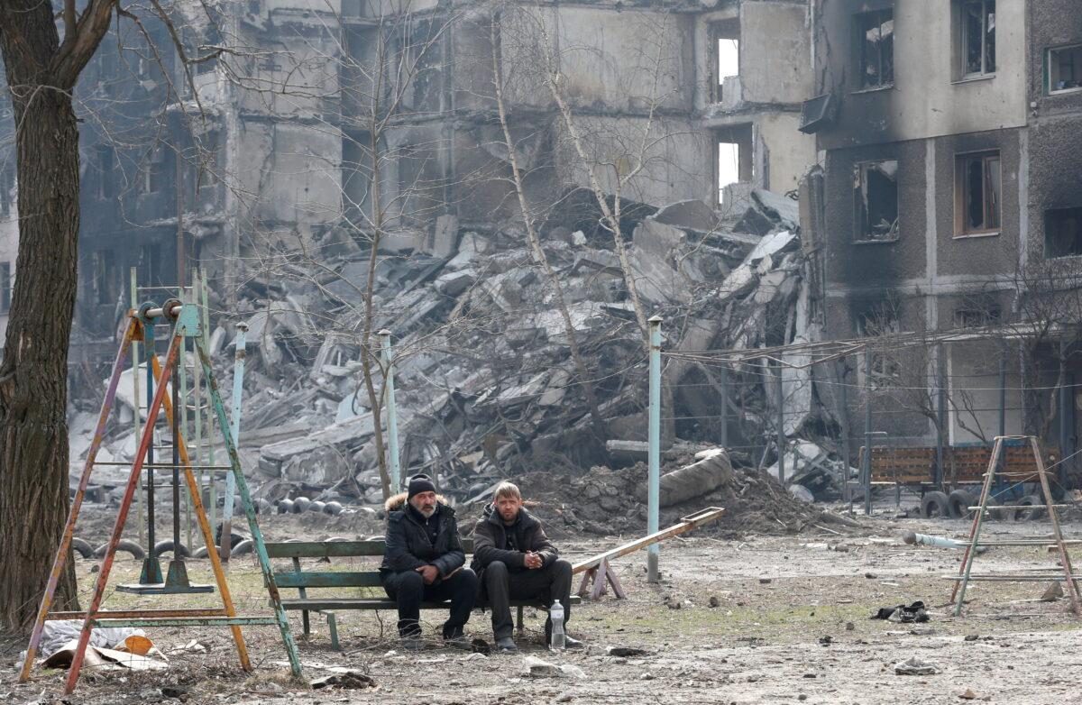 Local residents sit on a bench near an apartment building destroyed in the course of Ukraine–Russia conflict in the besieged southern port city of Mariupol, Ukraine, on March 25, 2022. (Alexander Ermochenko/Reuters)