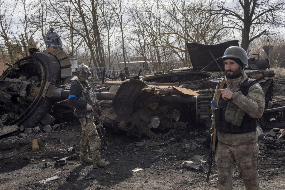 Ukranian servicemen walk past the wreck of a Russian tank in the village of Lukyanivka outside Kyiv, Ukraine, on March 27, 2022. (Marko Djurica/Reuters)