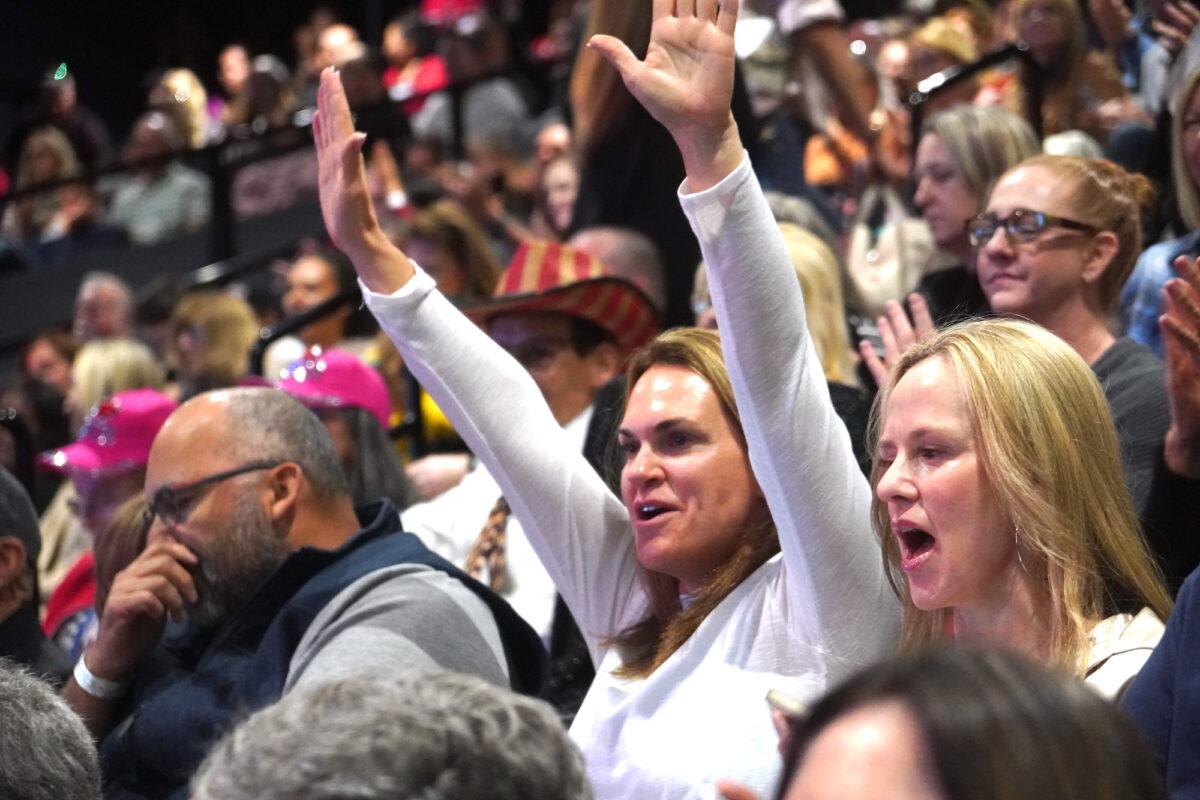 A woman raises her hands in victory during Clay Clark's "Reawaken America" tour stop in support of Christian conservative values in San Diego, on March 11. (Allan Stein/The Epoch Times)