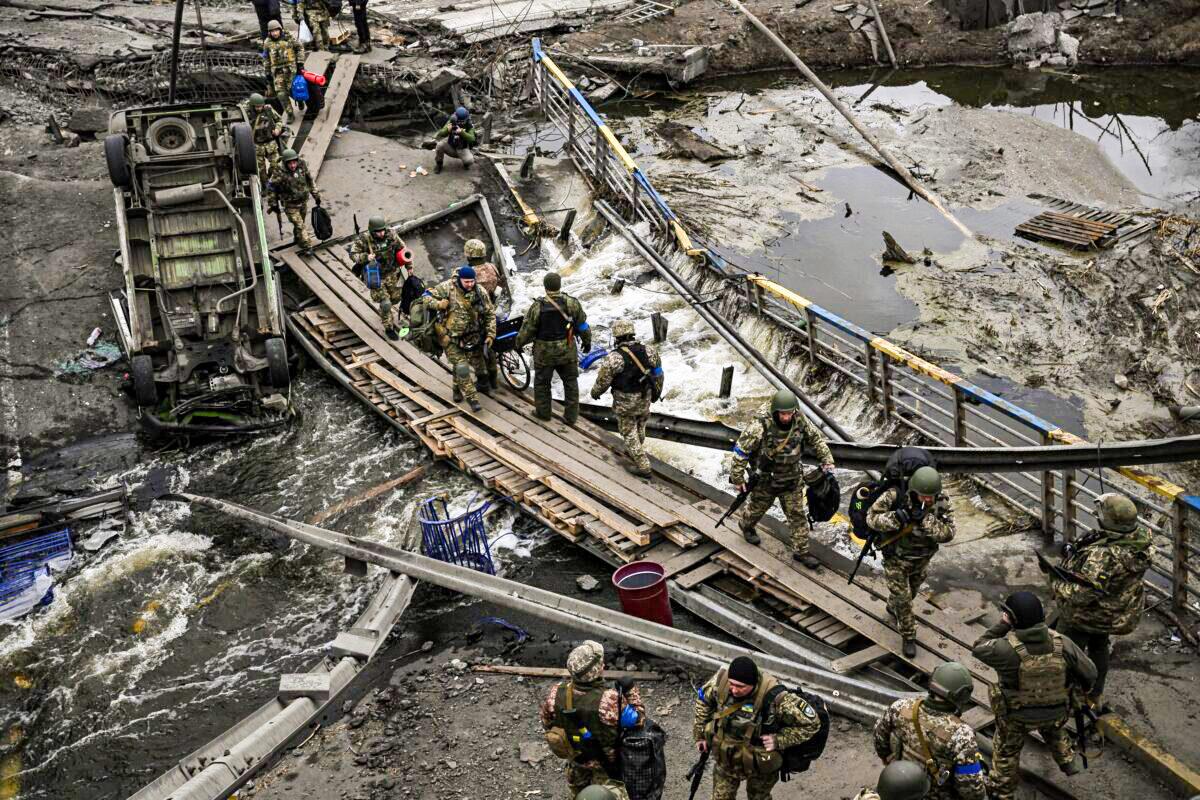 Ukranian servicemen walk on a makeshift pathway to cross a river next to a destroyed bridge near the city of Irpin, northwest of Kyiv, Ukraine, on March 13, 2022. (Aris Messinis/AFP via Getty Images)