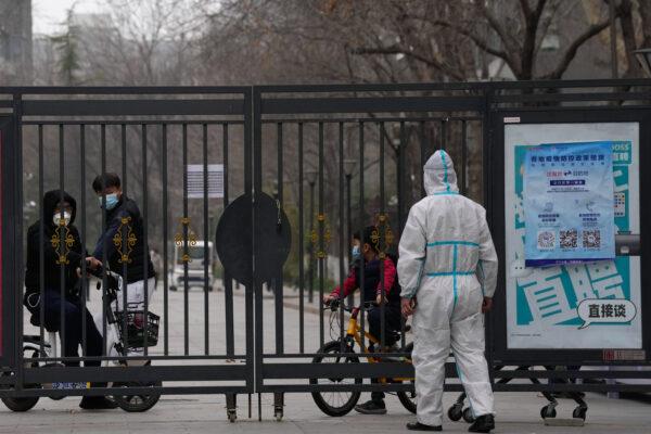 Residents in a locked-down community look out from a closed gate as a worker in protective gear monitors access on March 13, 2022, in Beijing. (Ng Han Guan/AP Photo)