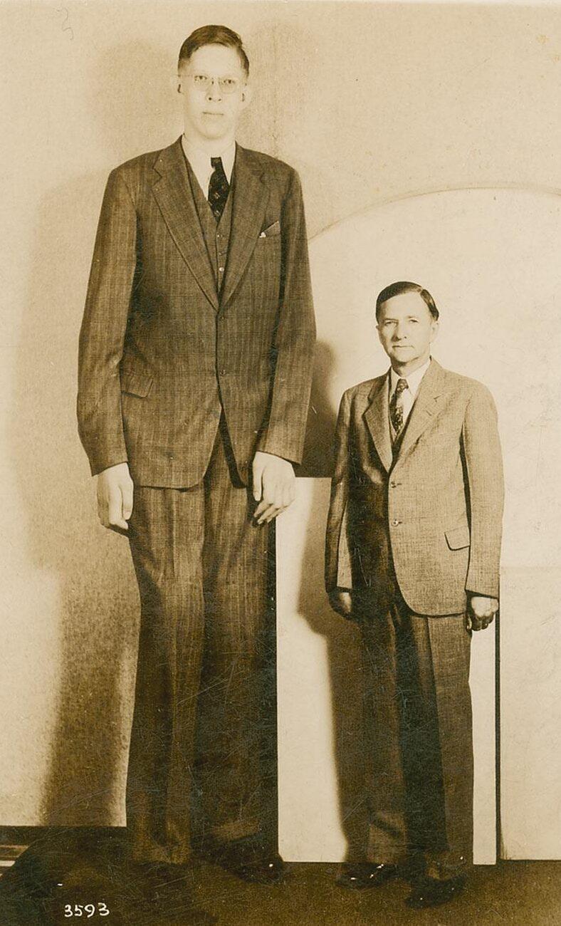 Robert Wadlow (L) beside his average-size father. (<a href="https://commons.wikimedia.org/wiki/File:Robert_Wadlow_postcard.jpg">Public Domain</a>)