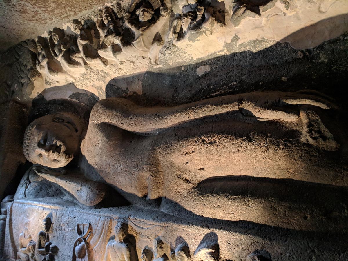 A large sculpture of a lying Buddha lines the wall of Ajanta Cave 26. It's said to represent Buddha at the moment of death prior to attaining Nirvana. Below are small sculpted figures mourning his death, while celestial beings rejoice from above. (Vengolis/ CC BY-SA 4.0)