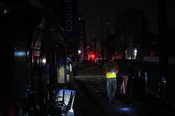 People walk along a street of a residential area during a power outage in Koto district in Tokyo early on March 17, 2022, after a powerful 7.4-magnitude quake jolted eastern Japan. (Philip Fong/AFP via Getty Images)