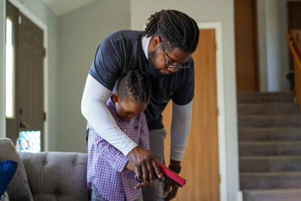 David Hayes teaches his 6-year-old son how to safely hold a training gun in their living room in Richton Park, Ill., on March 13, 2021. (Cara Ding/The Epoch Times)