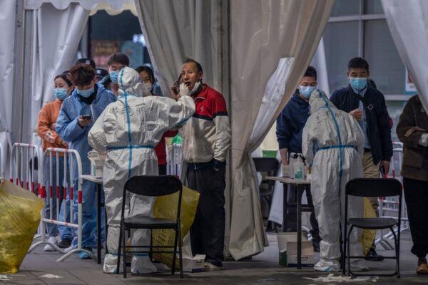 A medical worker wears protective clothing as a man talks on his mobile phone while he is swabbed for a nucleic acid test at a mass testing site in Beijing, China on March 15, 2022. (Kevin Frayer/Getty Images)