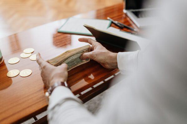 Stock photo of a people counting dollar notes on a table. (Karolina Grabowska/Pexels)