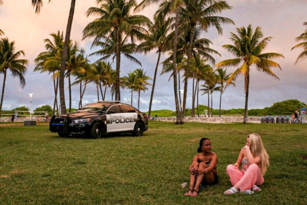 A police vehicle is seen next to people enjoying spring break, ahead of an 8pm curfew imposed by local authorities amid the COVID-19 pandemic, in Miami Beach, Florida, on March 27, 2021. (Marco Bello/Reuters)