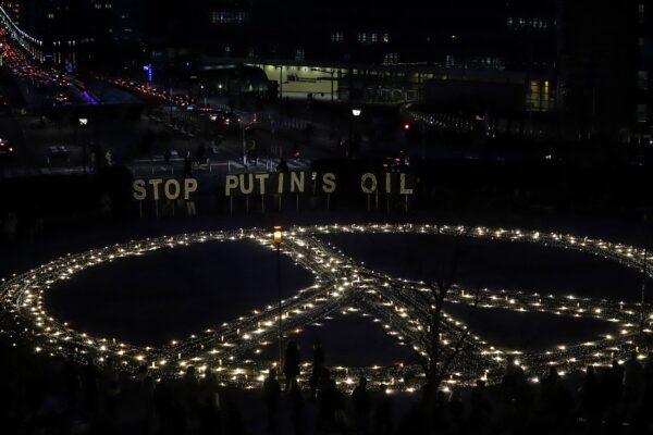 Avaaz members, demonstrators, and Ukrainian activists stand in front of signs reading "Stop Putin's oil" during a vigil for Ukraine near the European Union headquarters in Brussels on March 22, 2022. (Valeria Mongelli/AFP via Getty Images)