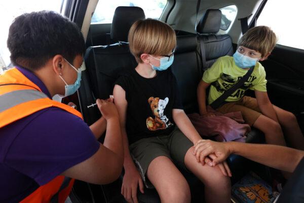 An 11-year-old boy is vaccinated as his brother looks on at a drive-through vaccination site at North Shore Events Centre in Auckland, New Zealand, on Jan. 17, 2022. (Fiona Goodall/Getty Images)