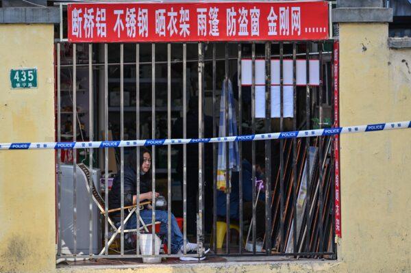  A person looks on from a closed shop next to a neighborhood in lockdown, as people are tested for COVID-19 in Shanghai on March 23, 2022. (Hector Retamal/AFP via Getty Images)