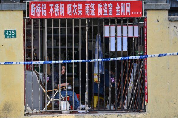 A person looks on from a closed shop next to a neighborhood in lockdown, as people are tested for COVID-19 in Shanghai on March 23, 2022. (Hector Retamal/AFP via Getty Images)