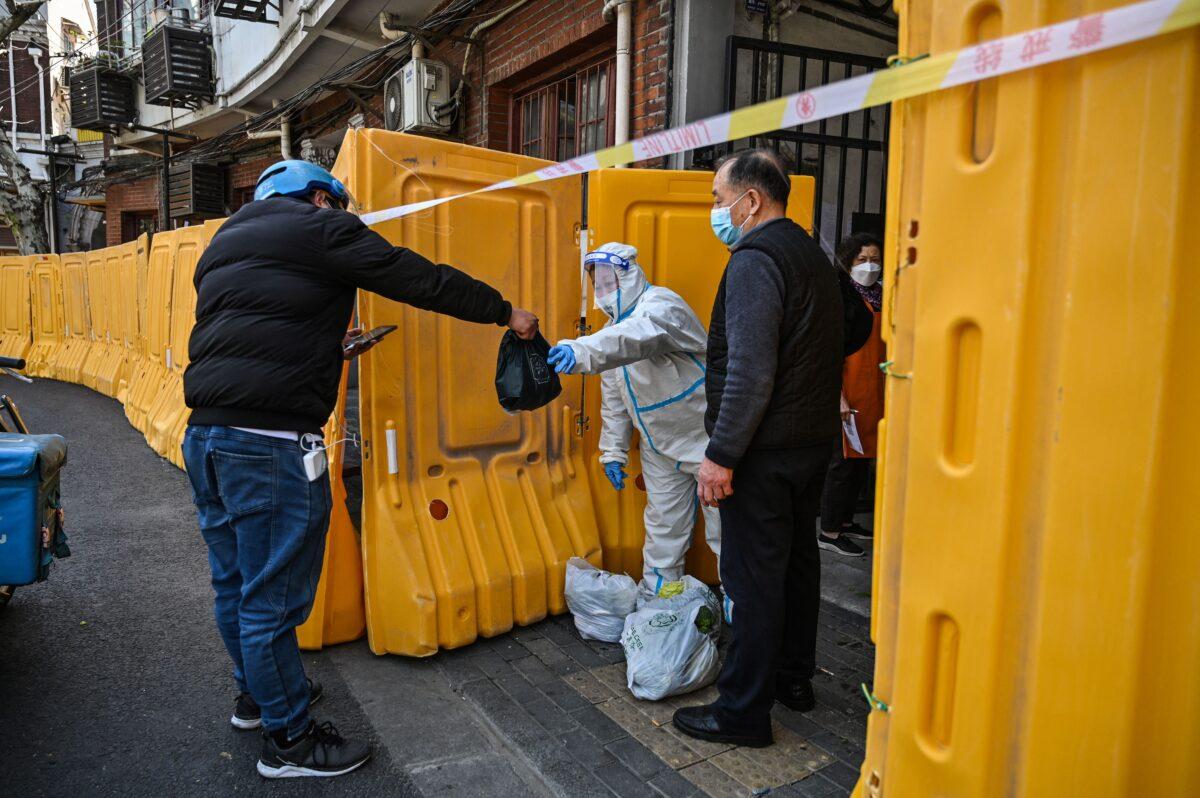 A worker in protective gear guards the entrance to a neighborhood in lockdown as a measure against COVID-19, receiving food from a delivery man in Jing'an district in Shanghai on March 29, 2022. (Hector Retamal/AFP via Getty Images)