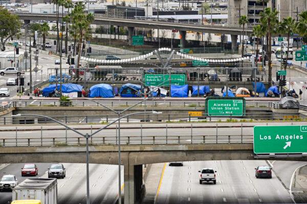 A man rides a bicycle in front of a row of homeless tents above a freeway in Los Angeles, on April 7, 2020. (Robyn Beck/AFP via Getty Images)