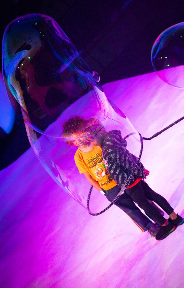 Artist Melody Yang wraps child volunteers within a bubble at Discovery Cube of Santa Ana, Calif., on March 31, 2022. (John Fredricks/The Epoch Times)