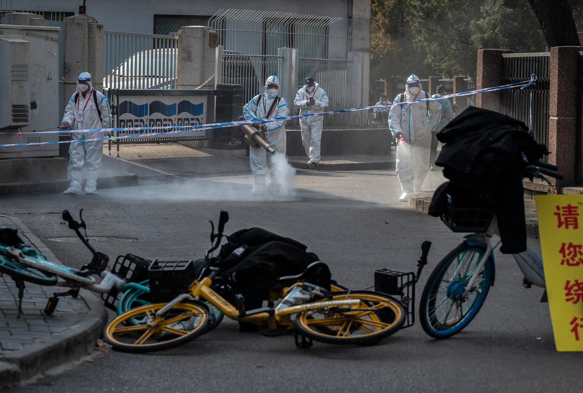 Health workers wear protective suits as they disinfect an area outside a barricaded community that was locked down for health monitoring after recent cases of COVID-19 were found in the area in Beijing, China, on March 28, 2022. (Kevin Frayer/Getty Images)