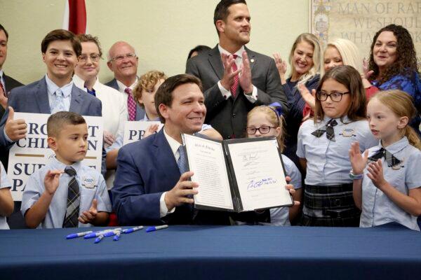 Florida Gov. Ron DeSantis displays the signed Parental Rights in Education bill, flanked by elementary school students, during a news conference at Classical Preparatory School in Shady Hills, Fla., on March 28, 2022. (Douglas R. Clifford/Tampa Bay Times via AP)