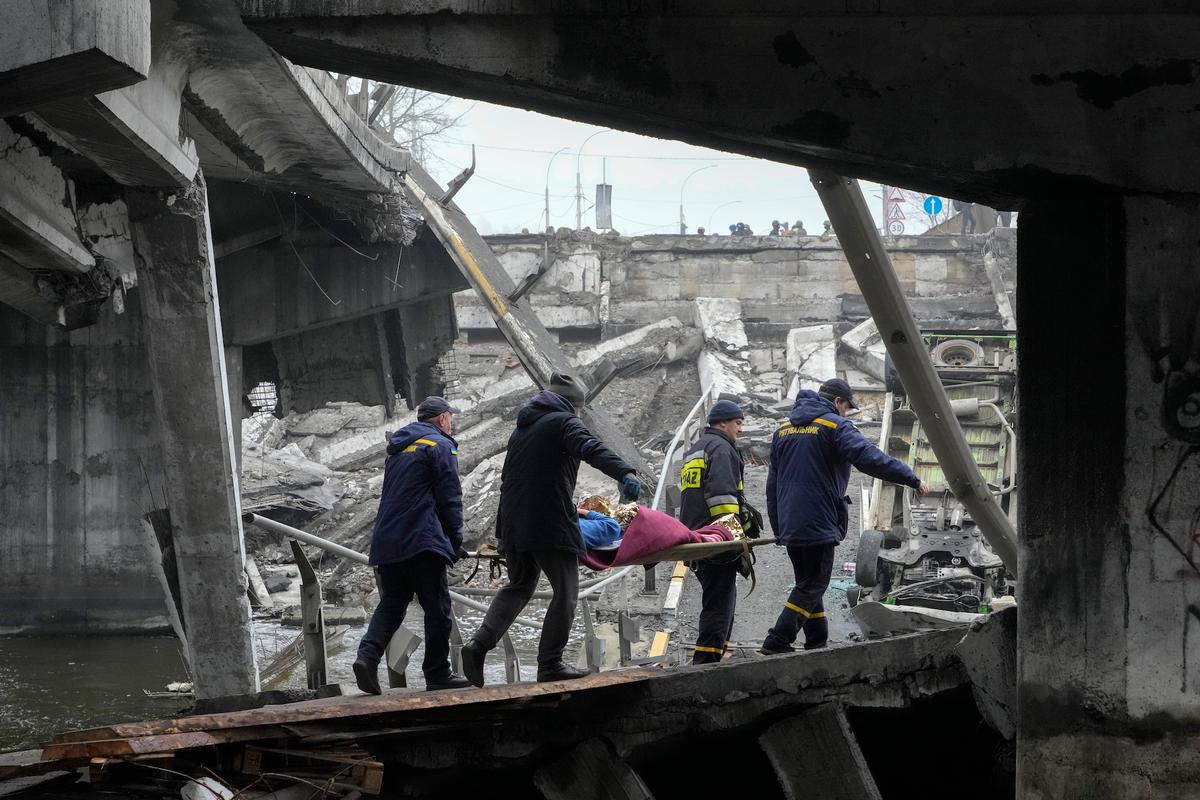 Ukrainian rescue workers carry an elderly woman under the destroyed bridge in Irpin, near Kyiv, Ukraine, on Apr. 1, 2022. (Efrem Lukatsky/AP Photo)