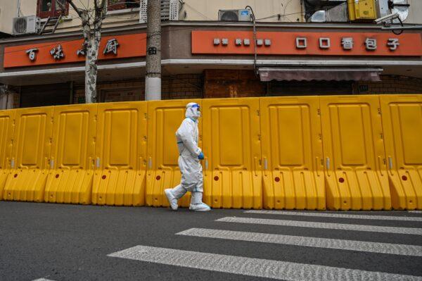 A worker wearing protective gear walks next to barriers that separate from the street, a neighborhood in lockdown as a measure against COVID-19 in Jing'an district in Shanghai on March 30, 2022. (Hector Retamal/AFP via Getty Images)