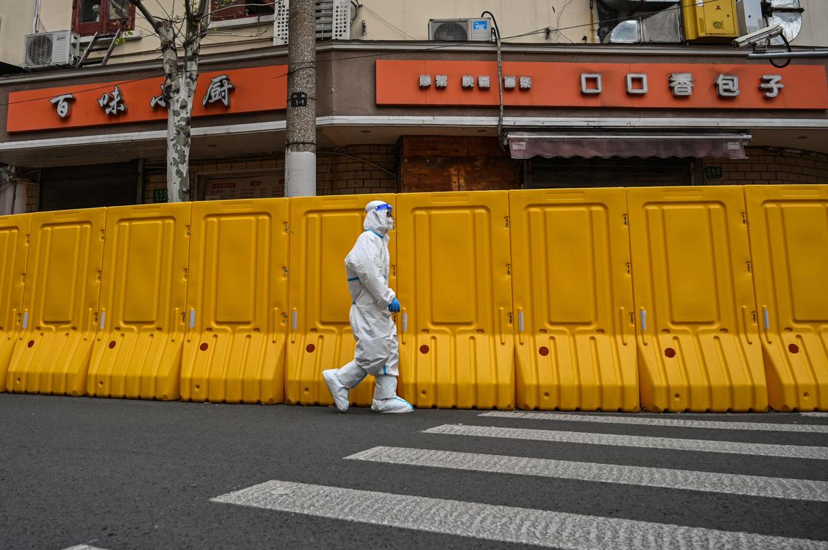 A worker wearing a protective gear walks next to barriers that separate from the street a neighborhood in lockdown as a measure against the Covid-19 coronavirus in Jing'an district, in Shanghai on March 30, 2022. (Hector Retamal/AFP via Getty Images)