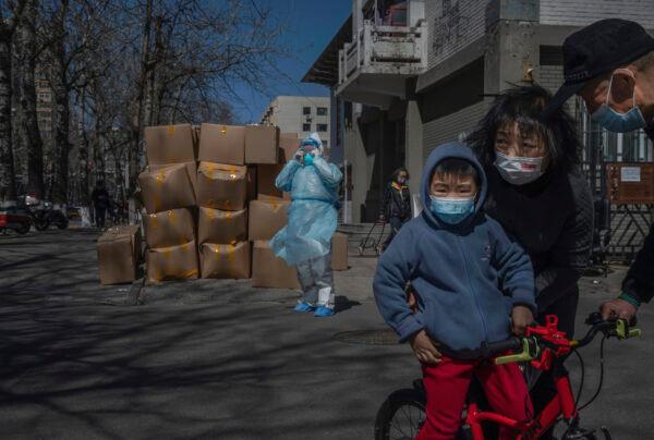 A woman pushes a child on his bike as a health worker wearing a protective suit loads medical waste on a truck to be removed from a community that was recently opened after it was locked down for health monitoring when cases of COVID-19 were found in the area, in Beijing, China, on March 31, 2022. (Kevin Frayer/Getty Images)