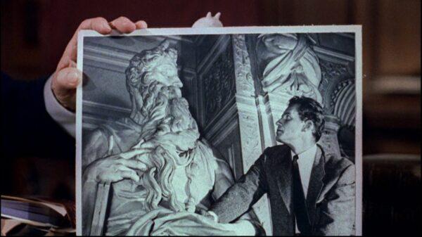 Cecil B. DeMille holds a photograph of Charlton Heston looking at Michelangelo's "Moses." Heston's resemblance to the sculpture helped him win the role of Moses in "The Ten Commandments." (Public Domain)